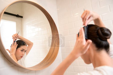 Foto de Young woman adjusting her hairstyles in bathroom at home , beauty wellness concept - Imagen libre de derechos