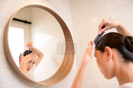 Foto de Young woman adjusting her hairstyles in bathroom at home , beauty wellness concept - Imagen libre de derechos