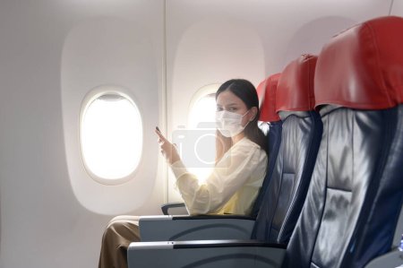 Foto de Una mujer joven con máscara facial está viajando en avión, Nuevo viaje normal después del concepto de pandemia covid-19 - Imagen libre de derechos