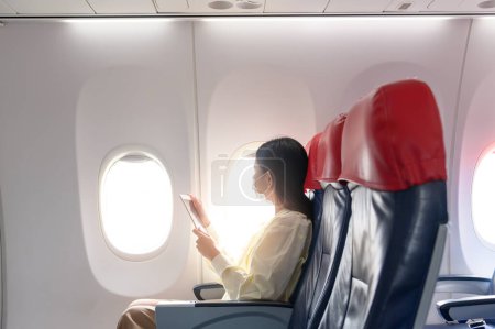 Foto de Una mujer joven con máscara facial está viajando en avión, Nuevo viaje normal después del concepto de pandemia covid-19 - Imagen libre de derechos