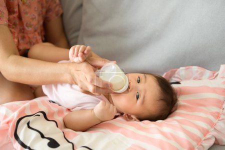 Téléchargez les photos : Une petite fille boit du lait concept de biberon, famille, enfant, enfance et parentalité - en image libre de droit