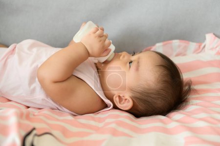 Téléchargez les photos : Une petite fille boit du lait concept de biberon, famille, enfant, enfance et parentalité - en image libre de droit