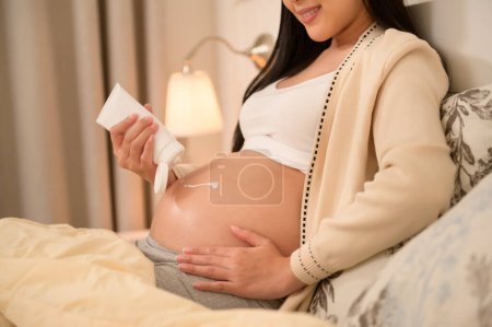 Beautiful pregnant woman applying moisturizing, stretch mark cream on belly, fertility infertility treatment, IVF, future maternity concept