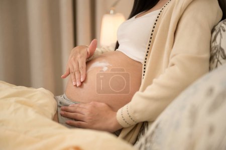 Beautiful pregnant woman applying moisturizing, stretch mark cream on belly, fertility infertility treatment, IVF, future maternity concept