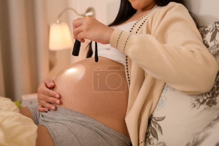 Hermosa mujer embarazada usando linterna en el vientre para estimular el desarrollo de un bebé, tratamiento de infertilidad de fertilidad, FIV, futuro concepto de maternidad 