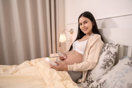 Téléchargez les photos : Belle femme enceinte tenant un doppler fœtal de poche pour écouter les battements de cœur du bébé sur le ventre, traitement de l'infertilité, FIV, concept de maternité futur - en image libre de droit