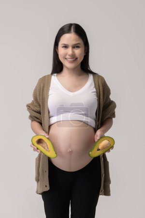 Téléchargez les photos : Portrait de Belle femme enceinte tenant avocat sur fond blanc studio, concept santé et maternité - en image libre de droit