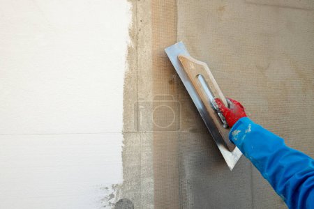Foto de Constructor enyesando la pared con una espátula, malla de fibra de vidrio, después de aislar la casa - Imagen libre de derechos