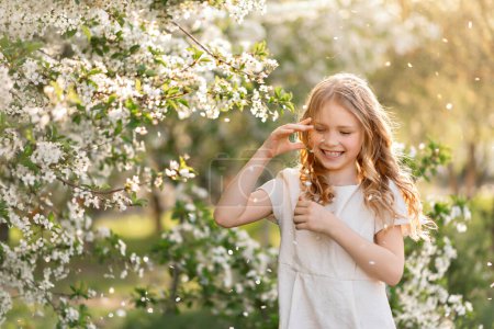 Foto de Beautiful child girl enjoying warm sunny spring weather at the blooming cherry trees garden under falling petals - Imagen libre de derechos