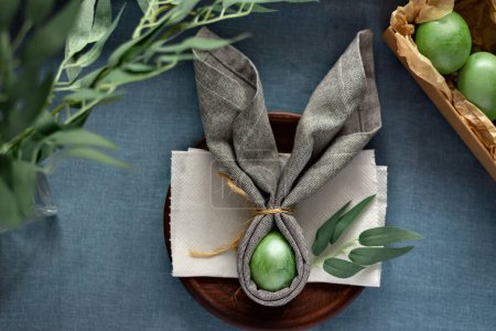 Foto de Aesthetic Easter table decoration, banny ears napkin and green dyed eggs on blue background, a spring holiday mockup with copy space - Imagen libre de derechos