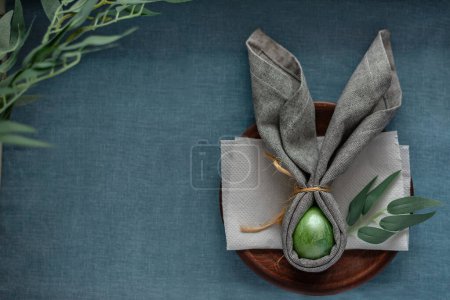 Foto de Happy Easter traditional holiday table decor, green colored egg with banny ears napkin on a blue background, spring template with copy space - Imagen libre de derechos