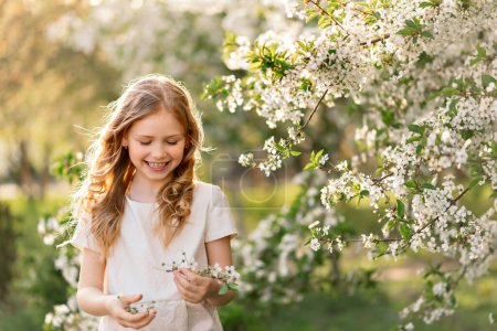 Foto de Feliz hermosa chica sonriendo y recoge flores en el jardín de cerezos florecientes primavera, espacio de copia - Imagen libre de derechos