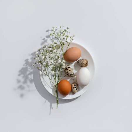 Foto de Elegant minimalist scandinavian Easter composition. Natural color eggs and flowers on a white plate. Aesthetic table setting, greeting card or banner template - Imagen libre de derechos