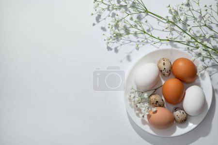 Foto de Ajuste de mesa minimalista estético de Pascua, huevos y flores en plato blanco, sobre fondo neutro. Plantilla o banner de primavera nórdico elegante, espacio de copia - Imagen libre de derechos