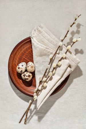 Téléchargez les photos : Aesthetic minimalist Easter decoration with quail eggs, pussy willow branches and napkin on a plate, on neutral beige linen background, rustic spring table setting, copy space - en image libre de droit