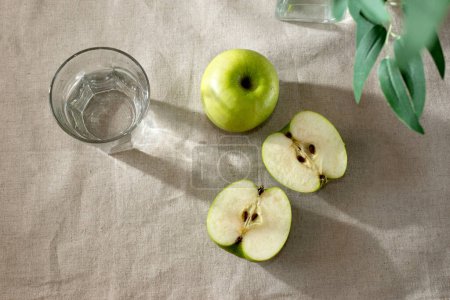 Photo for Green apples ang glass of water on a beige table, minimalist spring summer composition, copy space - Royalty Free Image