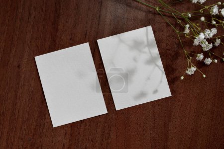 Foto de Tarjetas de hoja de papel en blanco con sombras florales sobre un fondo de superficie de mesa marrón oscuro, plantilla de marca clásica minimalista, espacio para copiar - Imagen libre de derechos