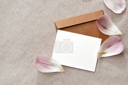 Téléchargez les photos : Délicate carte de vœux esthétique subtile, modèle d'invitation, carte papier vierge, enveloppe artisanale et pétales de fleurs sur fond beige neutre - en image libre de droit
