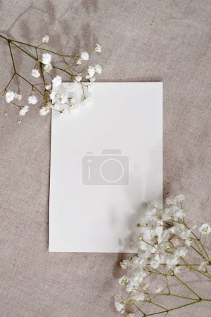 Téléchargez les photos : Carte de vœux esthétique minimale, modèle de lettre, carte de papier planche et fleurs sur un fond de lin beige neutre, espace de copie - en image libre de droit
