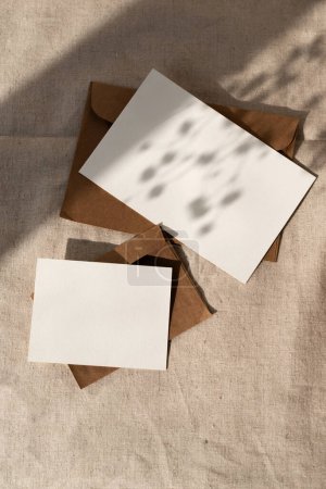 Plantilla de marca minimalista elegante, tarjeta de papel vacía y sobre con sombras de luz solar floral sobre un fondo textil beige neutro, maqueta estética, cama plana con espacio para copiar
