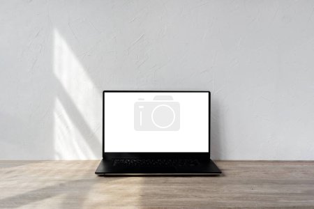 Photo for Laptop with blank screen mockup on a beige wooden table, geometric sunlight shadows on textured white wall, minimalist business, branding template, home interior design background - Royalty Free Image
