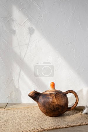 Téléchargez les photos : Théière minimaliste en céramique faite à la main sur une table en bois, ombres esthétiques à la lumière du soleil sur un fond de mur blanc, concept d'art poterie traditionnelle, espace de copie - en image libre de droit