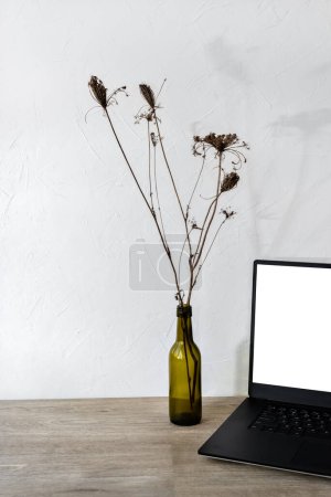 Téléchargez les photos : Modèle minimaliste de marque d'affaires avec espace de copie, ordinateur portable avec maquette d'écran vierge, bouquet de fleurs séchées dans un vase sur une table en bois, espace de travail à domicile - en image libre de droit