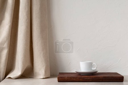 Foto de Taza de café blanco en un escritorio de madera marrón, cortina de lino beige neutro y mesa de piedra, fondo de pared blanco vacío, plantilla de diseño interior del hogar elegante minimalista con espacio de copia - Imagen libre de derechos