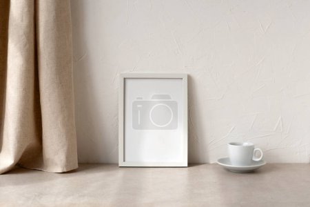 Foto de Marco de imagen vacío maqueta, taza de café en una mesa beige neutro, cortina de lino y fondo de pared blanca con luz solar, composición interior del hogar moderno, espacio de copia - Imagen libre de derechos