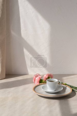 Photo for Aesthetic spring or summer floral composition with coffe cup and flowers on a beige tabletop, empty wall background with sun light shadows, morning lifestyle concept - Royalty Free Image