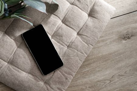 Téléchargez les photos : Téléphone portable avec maquette d'écran noir, modèle d'entreprise minimaliste esthétique style de vie avec smartphone sur un fond d'oreiller intérieur beige, espace de copie - en image libre de droit