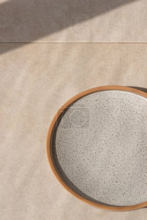 Foto de Fondo minimalista para publicidad de marca de restaurante o cafetería, plato vacío de cerámica gris neutro en una mesa de piedra beige con sombra de luz solar - Imagen libre de derechos