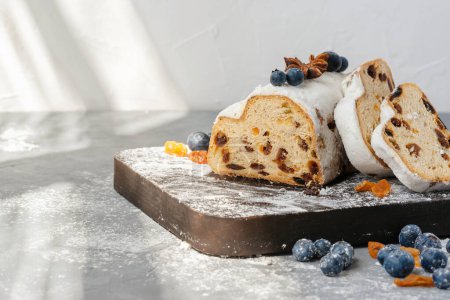 Photo for Lifestyle traditional Christmas stollen, sliced on a pieces on wooden board, in sunlight, winter holiday sweet dessert with raisins, blueberry and sugar powder icing - Royalty Free Image