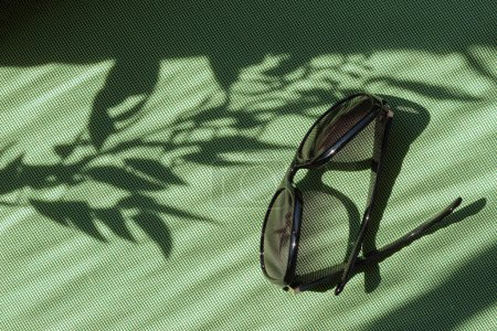 Foto de Gafas de sol sobre un fondo textil verde con sombra abstracta de luz solar floral, concepto de moda minimalista de verano, espacio para copiar - Imagen libre de derechos
