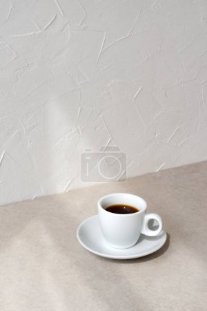 Téléchargez les photos : Tasse de café sur une table beige, mur blanc vide avec des ombres de lumière naturelle du soleil, fond minimaliste esthétique de marque d'affaires, espace de copie - en image libre de droit