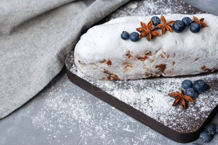 Téléchargez les photos : Christstollen, traditionnel Dresde Noël gonflé, pain de fruits festif décoré de myrtille, anis, sucre en poudre, raisins secs, sur une planche de bois sur un fond gris - en image libre de droit