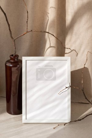 Photo for Empty picture frame on a table, vase with dried branches, beige linen curtain with abstract sunlight shadows pattern, aesthetic interior mock up with neutral background - Royalty Free Image