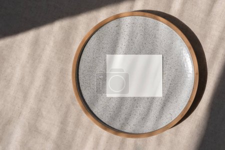 Photo for Minimalist business brand template, blank paper card mockup on ceramic plate, on a beige linen tablecloth background in sun light, wedding invitation or greeting card design - Royalty Free Image