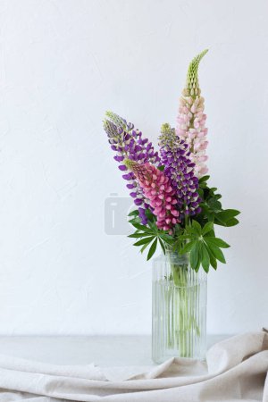 Téléchargez les photos : Bouquet d'été festif de fleurs violettes et roses en vase sur fond blanc neutre, nature morte florale intérieure esthétique avec lupin - en image libre de droit