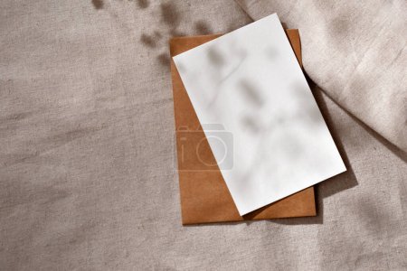 Foto de Tarjeta de hoja de papel vacía con espacio de copia simulada y sombras estéticas de luz solar floral en un mantel beige neutro - Imagen libre de derechos