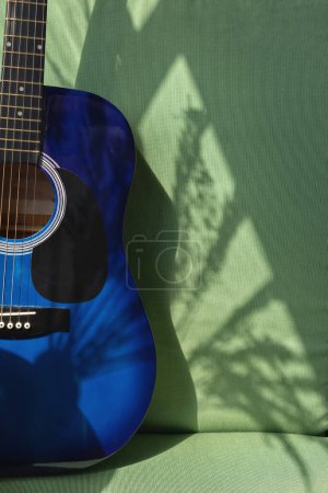 Photo for Blue guitar on a green chair background with aesthetic abstract sunlight shadow, music hobby, playing guitar learning at home concept - Royalty Free Image