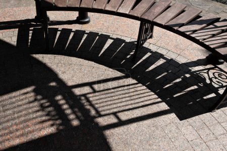Photo for Brown wooden bench and stone sidewalk pavement with a hard geometric sunlight shadow. Aesthetic modern garden house, courtyard, gazebo furniture, street architecture - Royalty Free Image