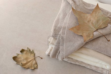 Téléchargez les photos : Pulls tricotés en laine empilés dans des couleurs neutres nues, feuilles d'automne brun clair sur une table beige. Armoire minimaliste de vêtements de mode, tricot jersey élégant - en image libre de droit