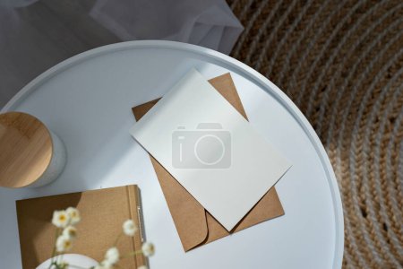 Foto de Tarjeta de papel en blanco maqueta, sobre, libro y flores en una mesa blanca a la luz del sol, boho estética interior naturaleza muerta, invitación a la boda, plantilla de marca de negocios - Imagen libre de derechos