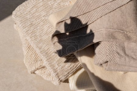 Foto de Suéteres de punto beige neutro sobre un fondo beige con silueta de sombra de luz solar de hoja de otoño estética. Otoño mujer ropa concepto de armario, estilo de vida - Imagen libre de derechos