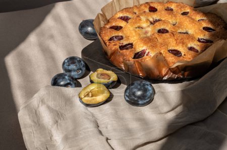 Photo for Homemade plum pie and plums on beige tablecloth with sunlight shadows. Sweet rustic bakery, traditional baked fruit cake, torte. - Royalty Free Image