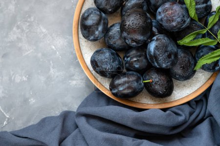 Foto de Ciruelas maduras en plato con gotas de agua, sobre mantel azul oscuro y fondo gris. Estético plano laico, primer plano, - Imagen libre de derechos