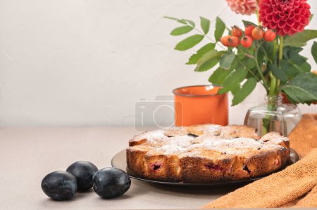 Foto de Pastel o pastel de ciruela americano tradicional, ciruelas, ramo de flores de otoño, taza en la mesa, con fondo blanco vacío de la pared. - Imagen libre de derechos