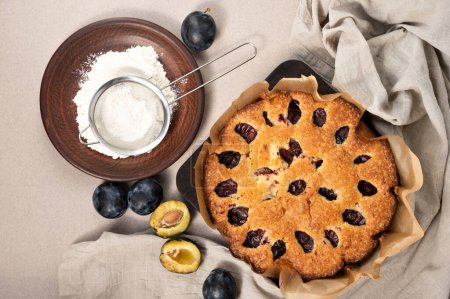 Téléchargez les photos : Une tarte aux prunes. Gâteau aux prunes, cannelle, sucre en poudre sur assiette, nappe en lin beige neutre. - en image libre de droit