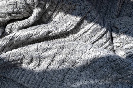 Photo for Natural lifestyle sunlight shadow on crumpled knitted neutral gray cloth with cable stitch pattern, cozy minimalist winter or fall background. - Royalty Free Image
